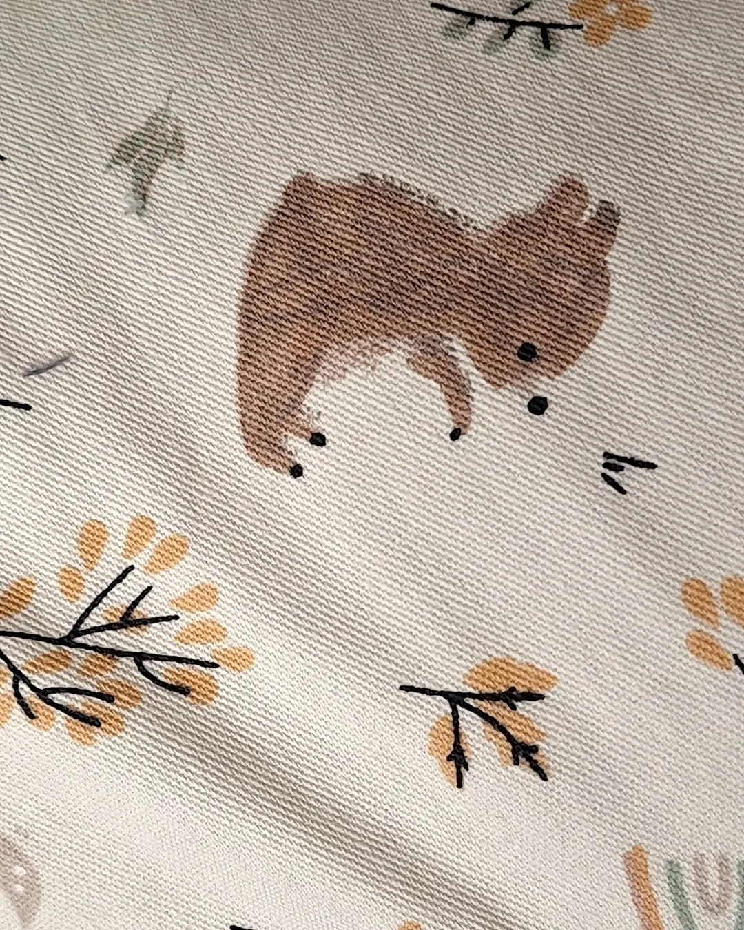 Detalle del estampado Rabbit del almohadón de lactancia, oso marrón y ramitas mostaza sobre algodón crema.